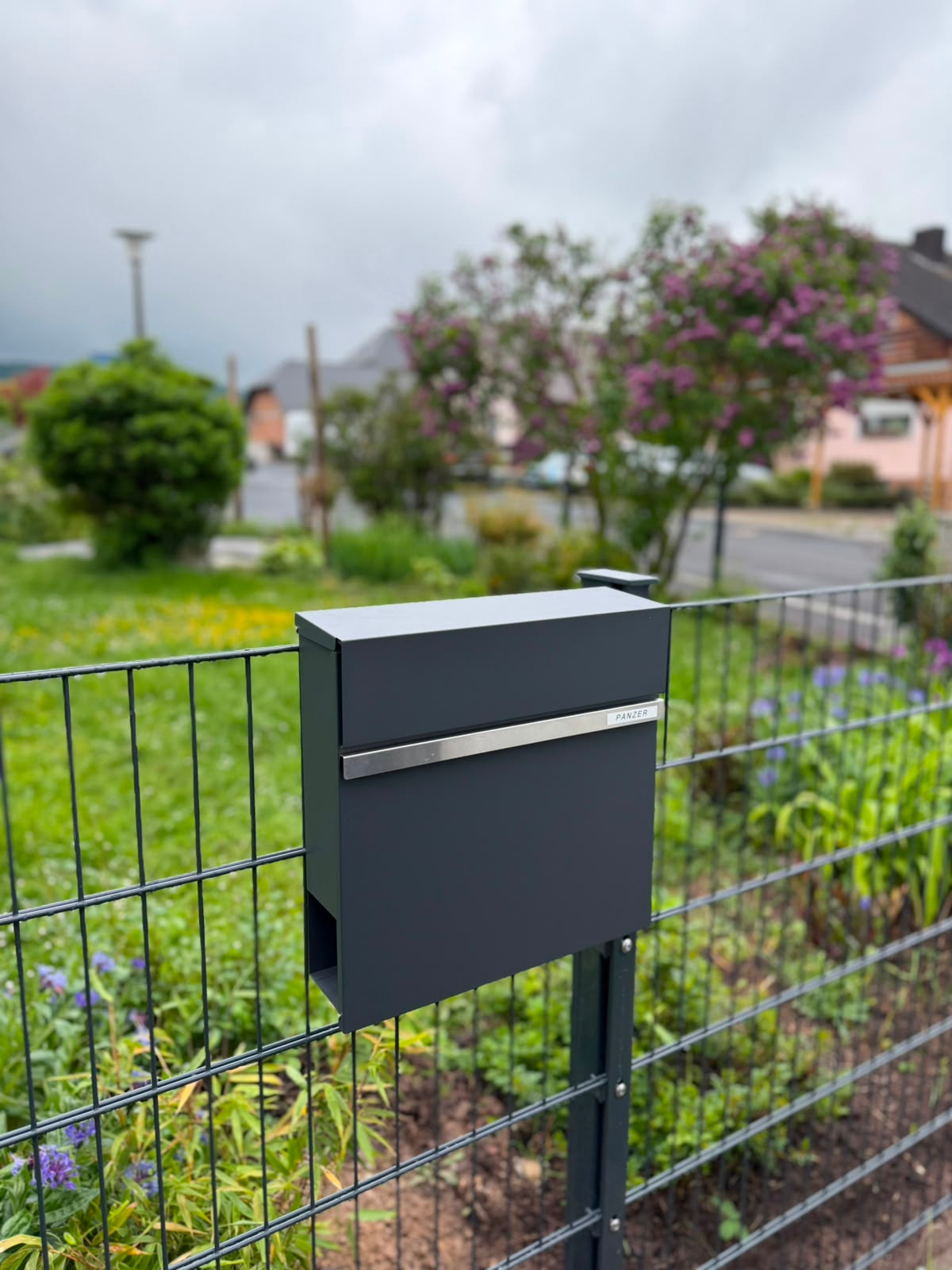 Schwarze Zaunanlage an einem modernen Kiesbeet mit Formgehölz und Sitzbank – klare Linien im gepflegten Gartenbereich.