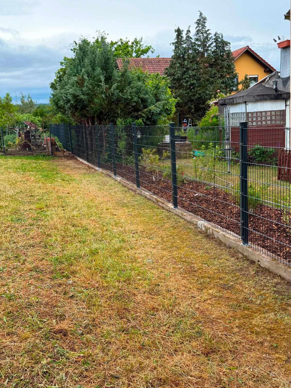Vorgartenabgrenzung neben der Garage – Doppelstabmatte vor gepflegter Hecke und heller Fassade.